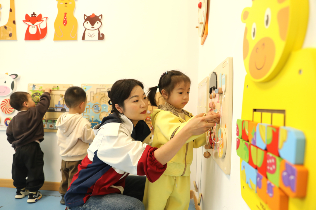 4月24日，天柱县妇幼保健院托育中心内，保育员正耐心引导幼儿操作墙面益智玩具。.JPG