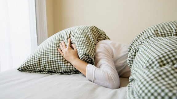 Lady cover her head by pillow on a bed 